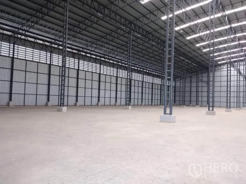 Factory for rent in Mueang Samut Prakan, Samut Prakan - Angled view of large warehouse bay with steel columns, louvered ventilation panels and bright lighting.
