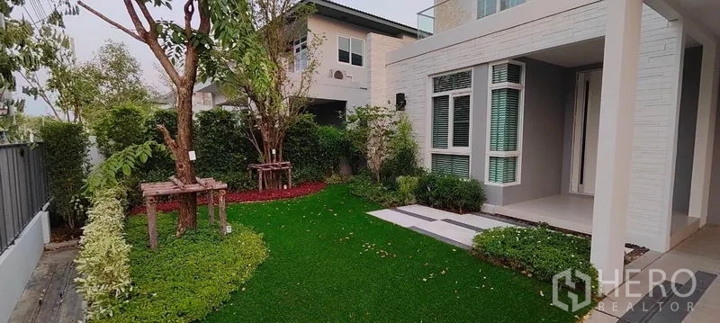 Detached House for rent in Prawet, Bangkok - Landscaped front garden with trimmed lawn, trees, and a sheltered porch.