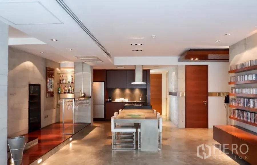 Condominium for rent or sale in Khlong Toei, Bangkok - Open-plan living and kitchen with concrete island, built‑in bar, wood accents and shelving.