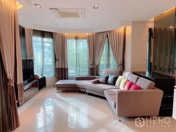 独立式住宅 出租或出售在Prawet, Bangkok - 转角起居区，落地窗与纱帘，L形沙发对着电视墙。