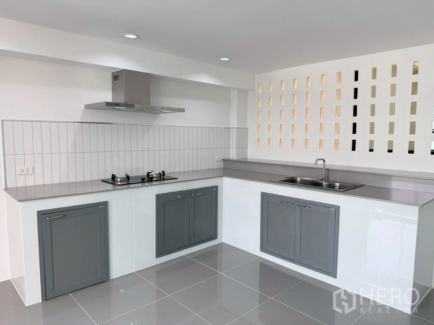 Townhouse for sale in Phra Khanong, Bangkok - L-shaped kitchen with gas hob, hood, ample counters, and grey cabinetry.