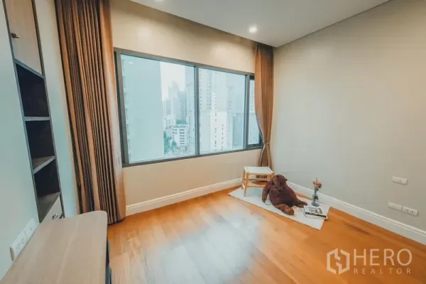 Condominium for rent in Khlong Toei, Bangkok - Spacious room with large window offering city skyline views and warm wood floors.