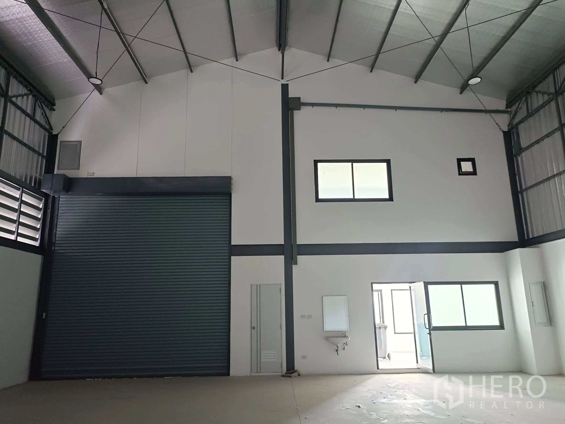 Warehouse for rent or sale in Bang Yai, Nonthaburi - Warehouse bay showing oversized roller shutter, internal windows, sink and doorway to restroom and office.