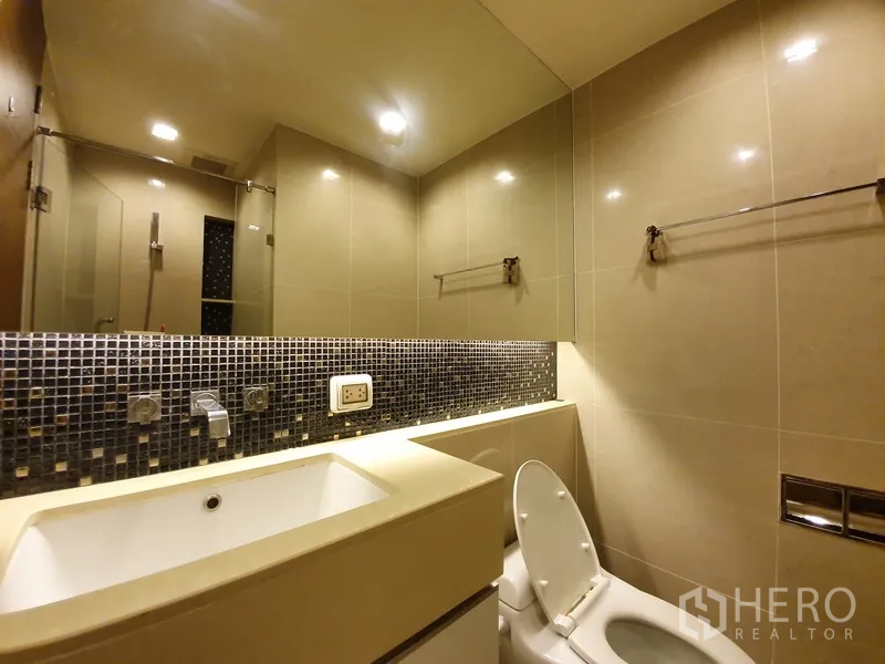 Condominium for rent in Bang Rak, Bangkok - Modern guest bathroom with mosaic backsplash, vanity sink, and toilet.