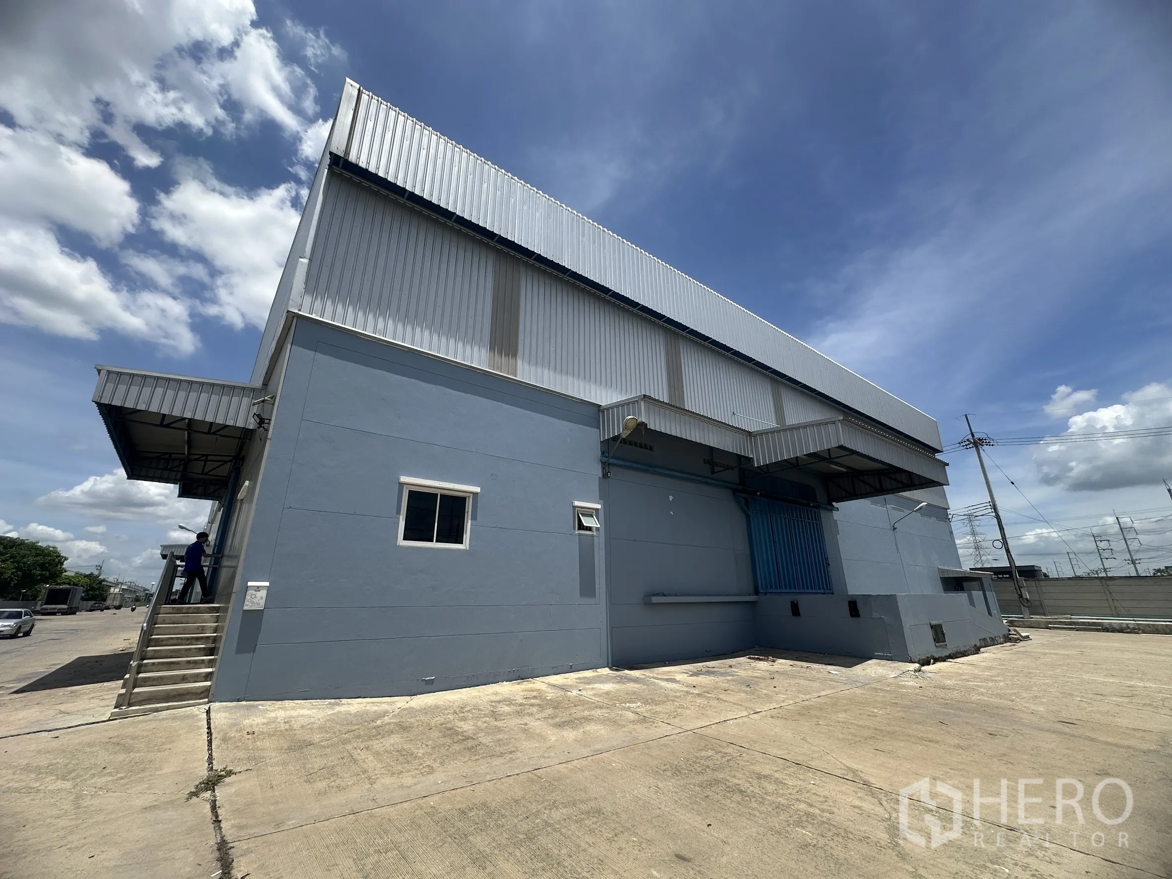 Warehouse for rent in Lat Lum Kaeo, Pathum Thani - Warehouse side view showing exterior stairs to a door and a sheltered loading bay with a roller door.