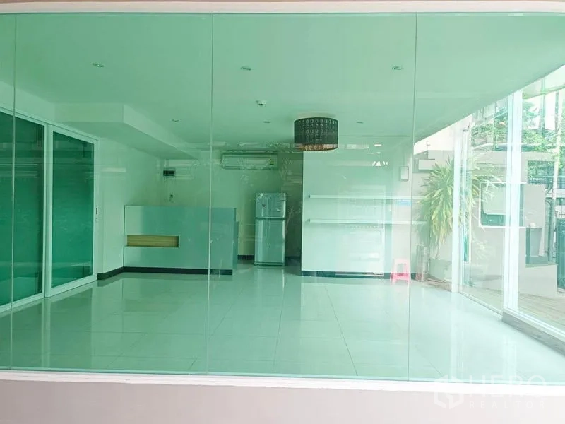 Retail Space for rent - Open-plan shop interior viewed through glass façade with shelves, counter and greenery.