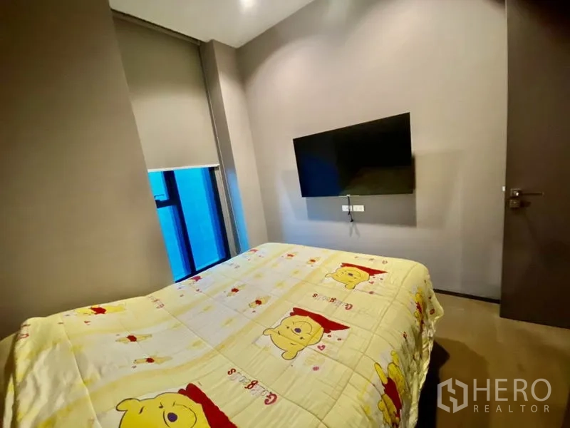 Condominium for rent or sale in Bang Rak, Bangkok - Second bedroom with wall-mounted TV, window and blackout blinds.