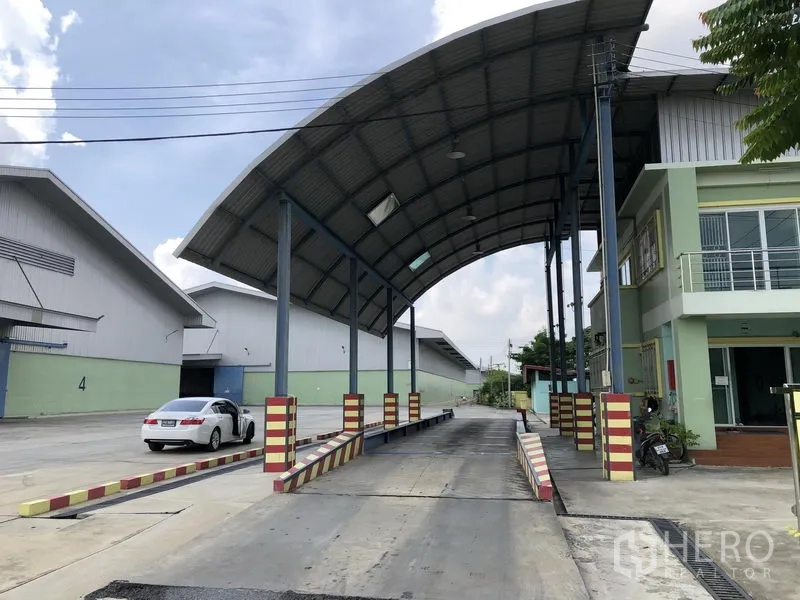 Warehouse for rent in Phra Nakhon Si Ayutthaya - Entrance of an industrial warehouse complex with arched canopy, covered truck scale and office beside a wide concrete driveway.
