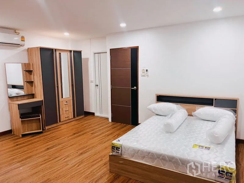 Townhouse for rent in Huai Khwang, Bangkok - Spacious bedroom with wood flooring, double bed, wardrobe and dressing table.