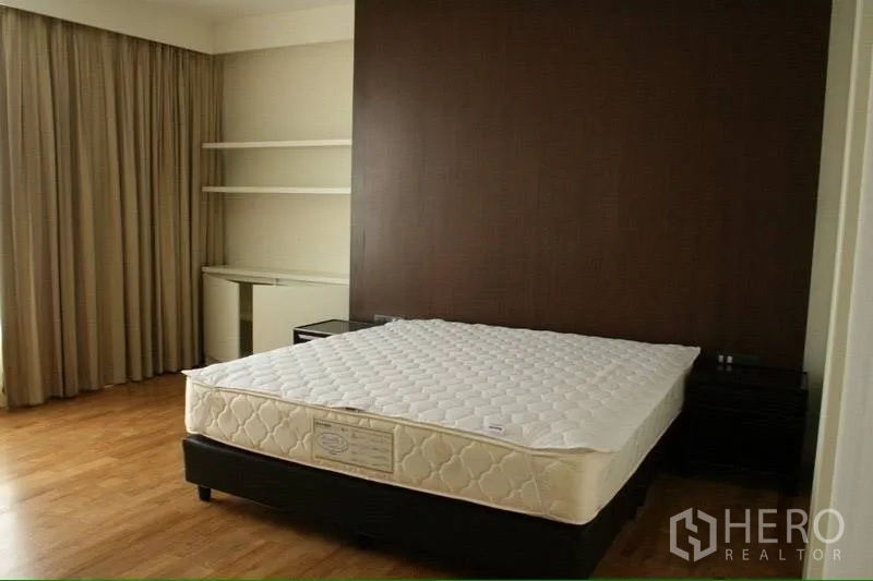 Condominium for rent in Watthana, Bangkok - Spacious bedroom with wood floors, dark feature wall, built-in desk and shelves, and a large curtained window.