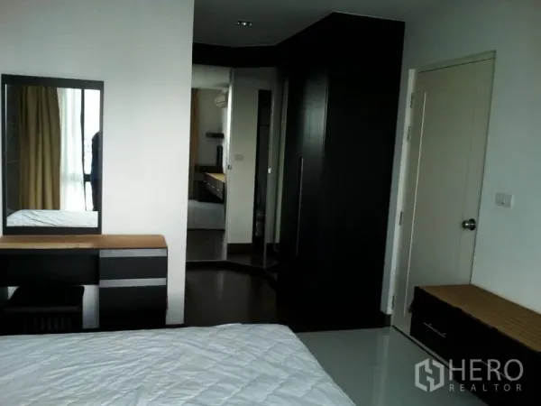 公寓 出租在Watthana, Bangkok - 主卧配梳妆台与镜子，内置衣柜与深色木质家具。