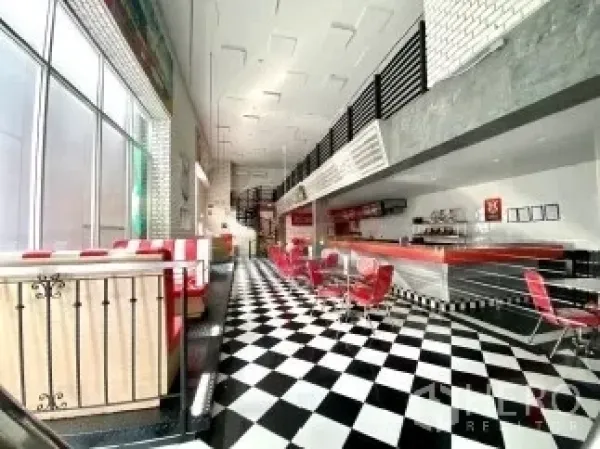 零售空间 出租在Watthana, Bangkok - 明亮的零售室内，黑白棋盘地砖、红色吧台座椅、挑高天花与落地窗。