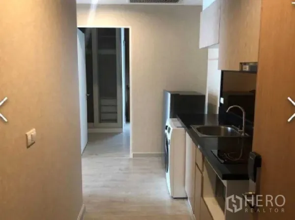 Condominium for rent in Watthana, Bangkok - Galley kitchen with black stone countertop, sink, upper cabinets and a washing machine.