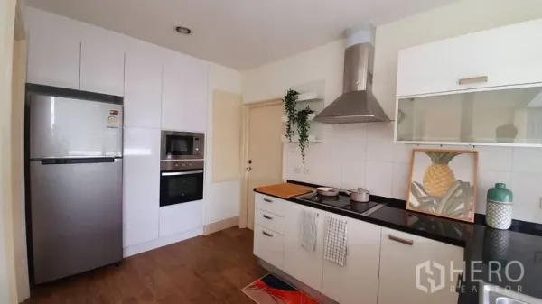 Condominium for rent in Watthana, Bangkok - Bright modern kitchen with white cabinetry, black counters, range hood and stainless appliances.