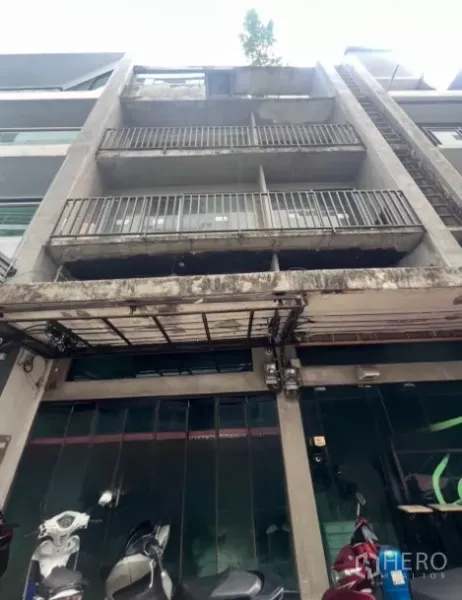 Shophouse for sale - Four-storey concrete shophouse facade with balconies and a glass storefront in Bangkok.