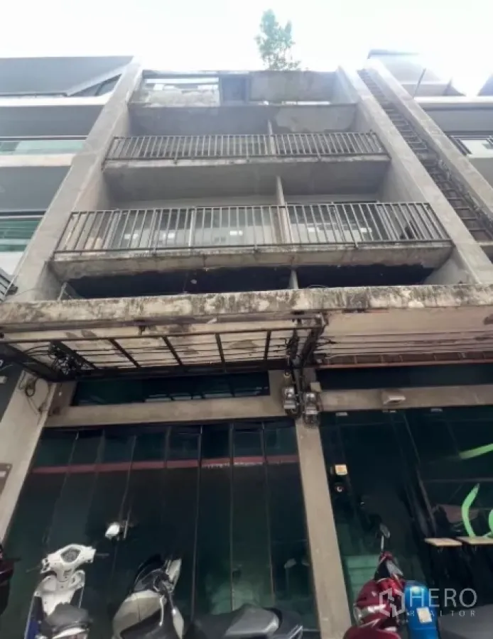 Shophouse for sale - Four-storey concrete shophouse facade with balconies and a glass storefront in Bangkok.