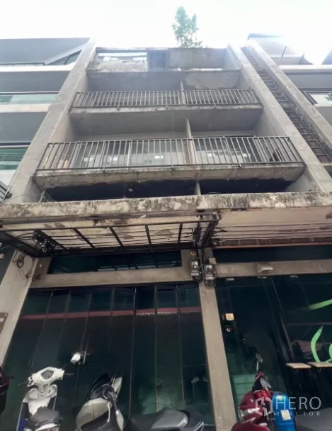 Shophouse for sale - Four-storey concrete shophouse facade with balconies and a glass storefront in Bangkok.