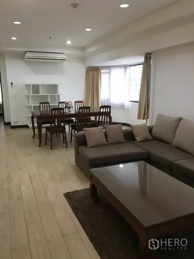 公寓 出租在Watthana, Bangkok - 瓦他那区公寓的开放式客餐厅，木地板，转角沙发与大窗，近BTS澎蓬站