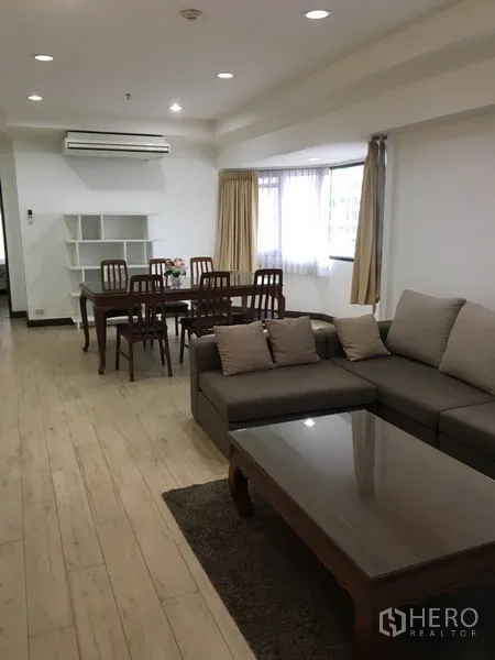 公寓 出租在Watthana, Bangkok - 瓦他那区公寓的开放式客餐厅，木地板，转角沙发与大窗，近BTS澎蓬站
