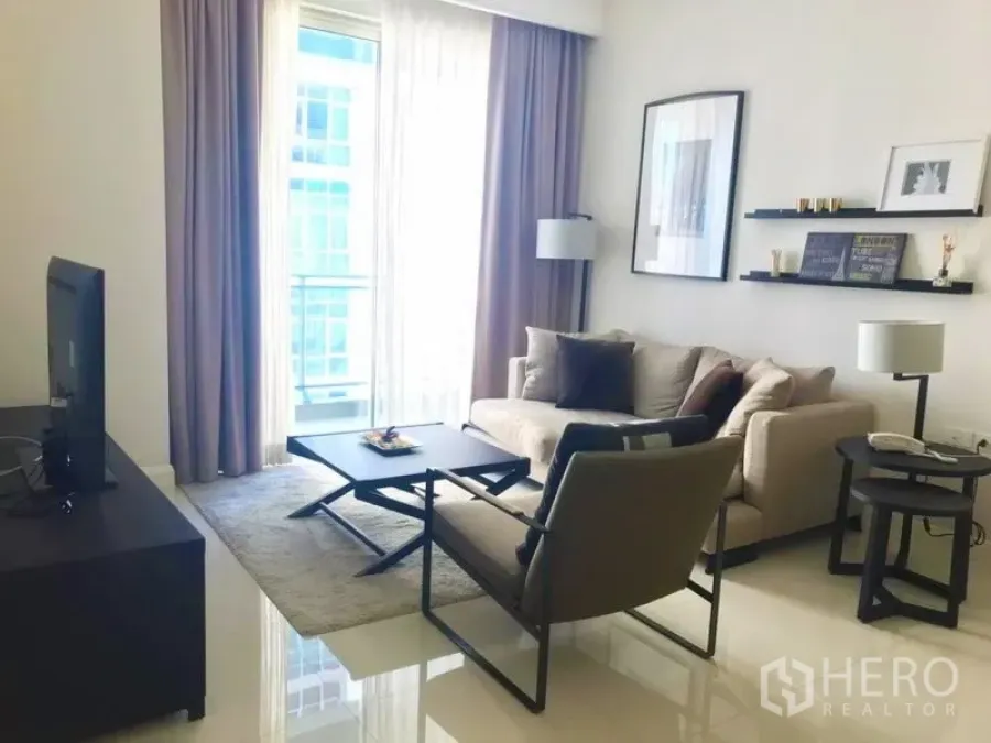 คอนโด ให้เช่าในPathum Wan, Bangkok - ห้องนั่งเล่นสว่างพร้อมโซฟา เก้าอี้เดี่ยว ชุดทีวี และระเบียงผ้าม่านบาง ในคอนโดสมัยใหม่