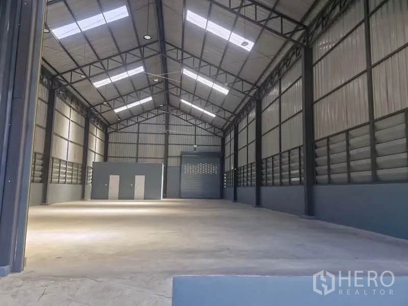 工厂 for rent in Khlong Luang, Pathum Thani - 宽敞厂房大厅，挑高人字顶钢结构，采光天窗、混凝土地面与卷闸门。