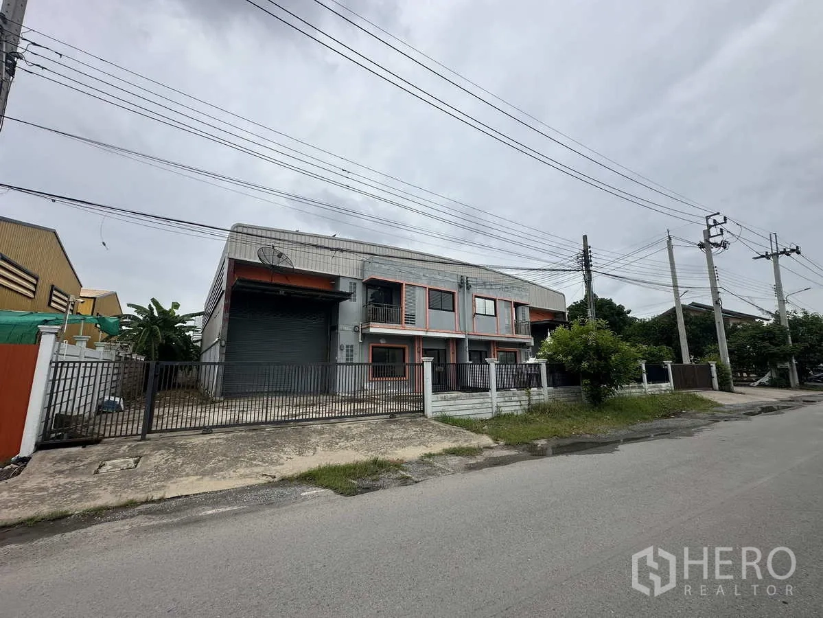 Warehouse for rent or sale in Bang Yai, Nonthaburi - Street view of the warehouse exterior with fence, driveway and utility poles.
