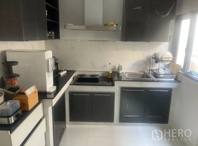 Detached House for rent or sale in Saphan Sung, Bangkok - L-shaped kitchen with black cabinetry, cooktop, hood and window.