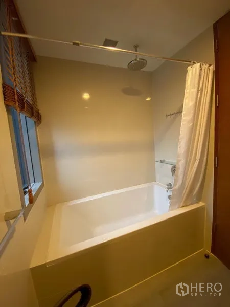 Condominium for rent in Khlong Toei, Bangkok - Bathroom with deep soaking tub, rainfall shower and a window with blinds.