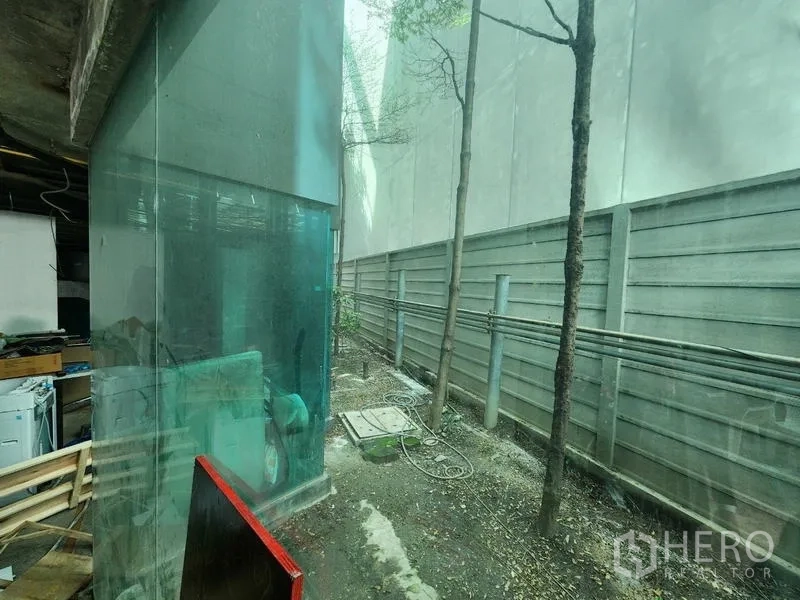 零售空间 出租 - 玻璃转角与狭长服务庭院，靠墙有树木与管线。