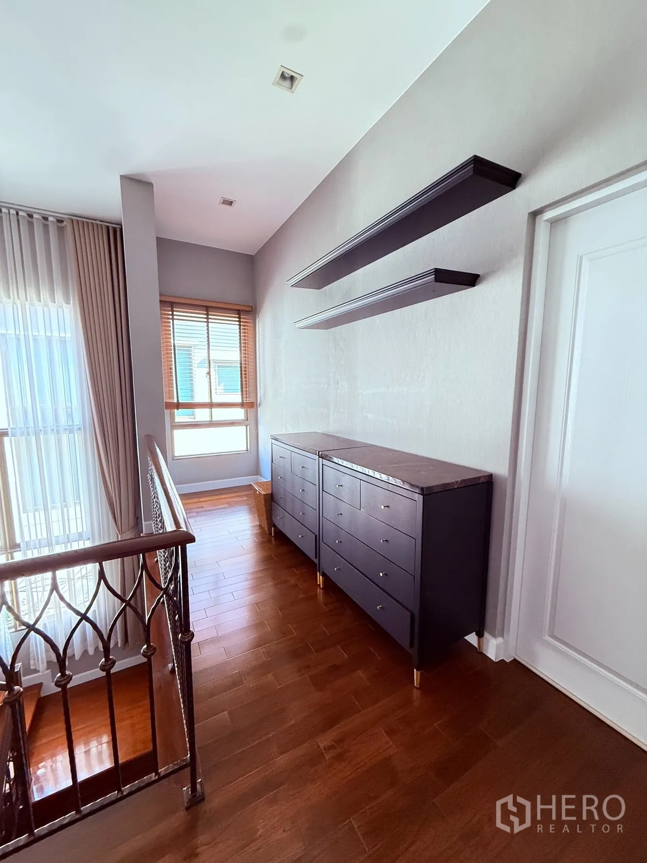 Detached House for rent or sale in Prawet, Bangkok - Upstairs landing with wooden floor, railing, drawers, and floating wall shelves.