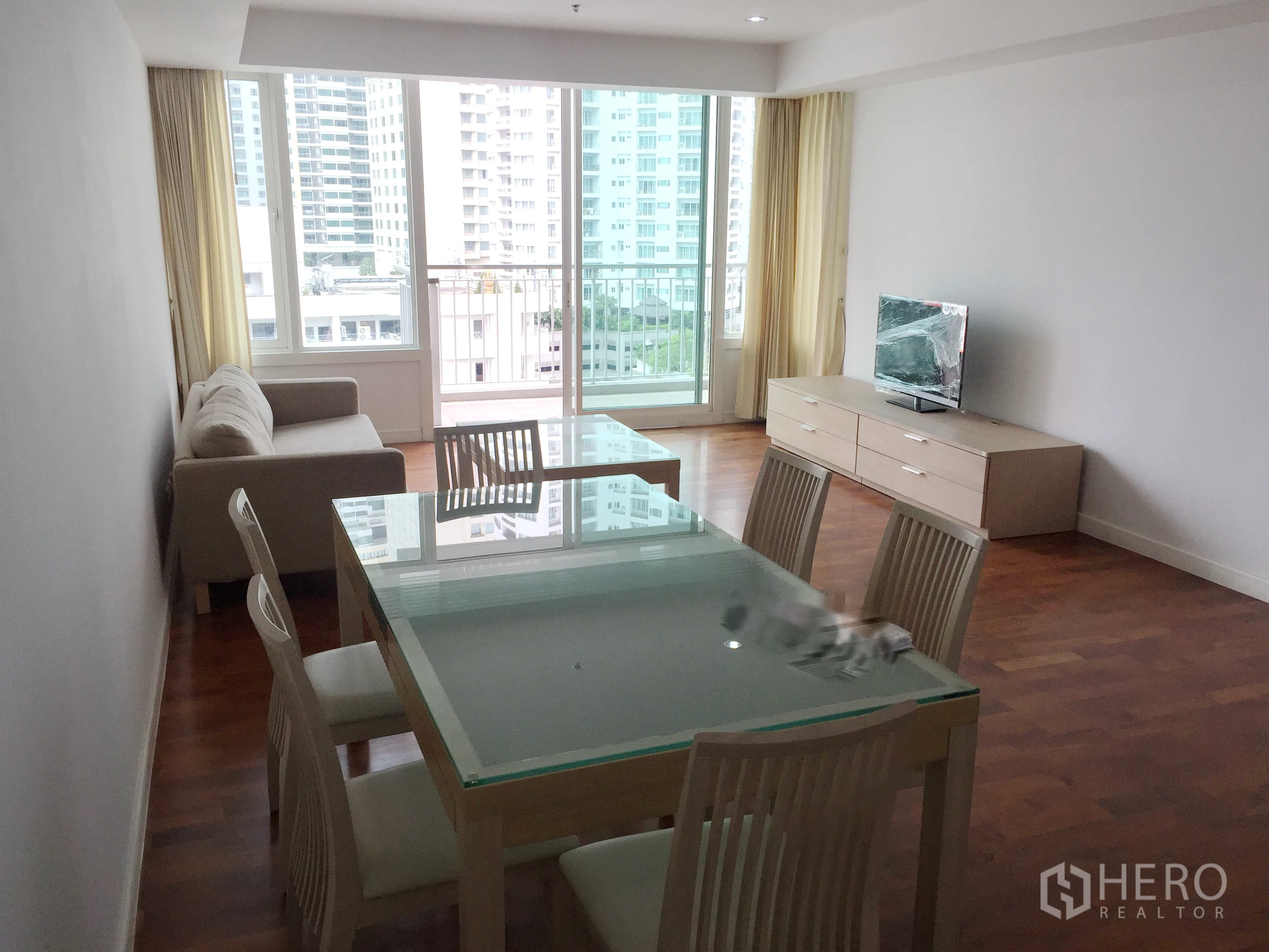 Condominium for rent in Khlong Toei, Bangkok - Open-plan living and dining room with glass-top table, sofa, TV console, and balcony city view.