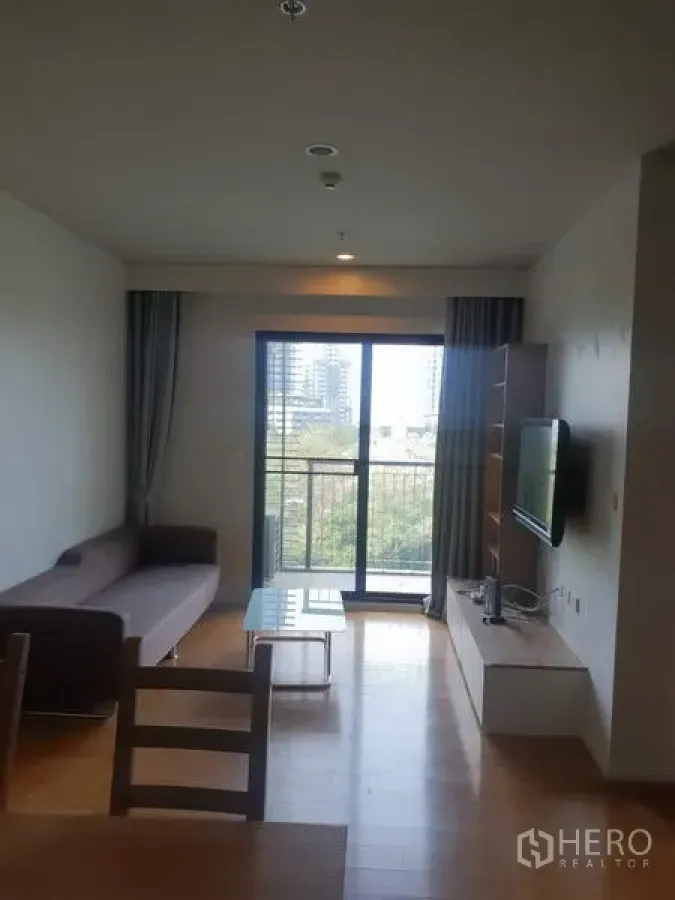 คอนโด ให้เช่าในWatthana, Bangkok - ห้องนั่งเล่นสว่าง โซฟา ทีวี และประตูกระจกเปิดสู่ระเบียงวิวต้นไม้