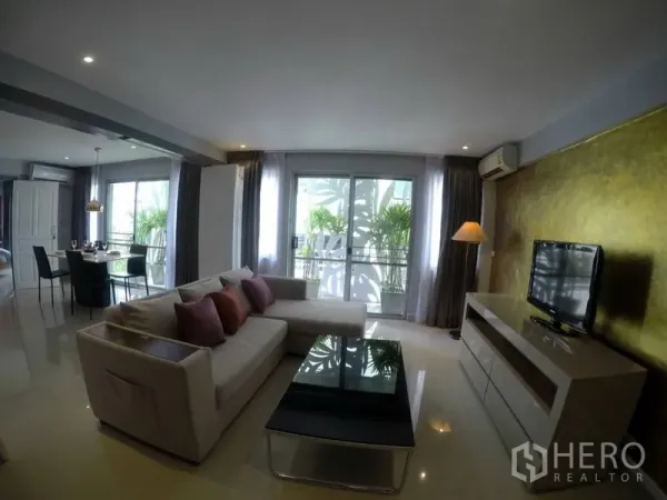 公寓 出租在Watthana, Bangkok - 客厅配L型沙发与电视柜，玻璃门通向阳台。