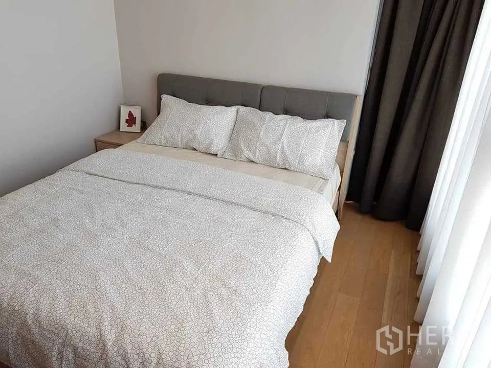 Condominium for rent in Khlong Toei, Bangkok - Second bedroom with upholstered headboard, bedside table and floor-to-ceiling curtains.