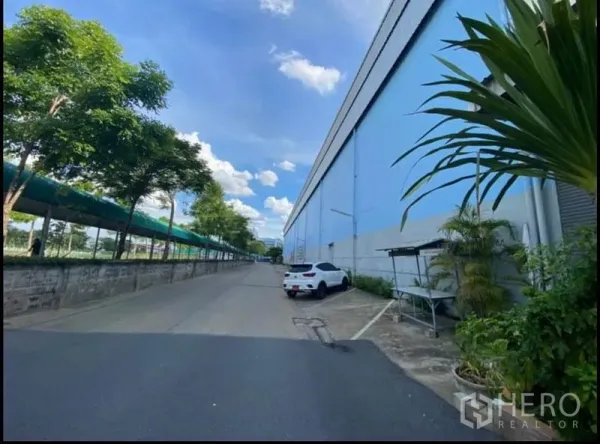 คลังสินค้า ให้เช่าในSai Mai, Bangkok - ด้านข้างอาคารโกดังยาว มีรถจอดและถนนบริการเรียงต้นไม้ เหมาะสำหรับรถบรรทุก