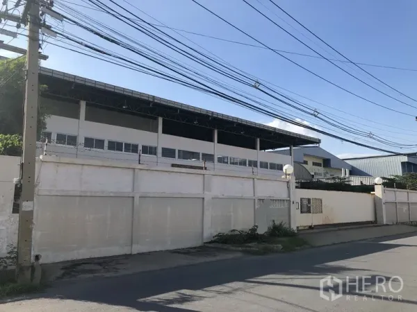 Factory for sale in Khlong Luang, Pathum Thani - Street view of a walled factory complex with tall steel roof behind the perimeter wall.
