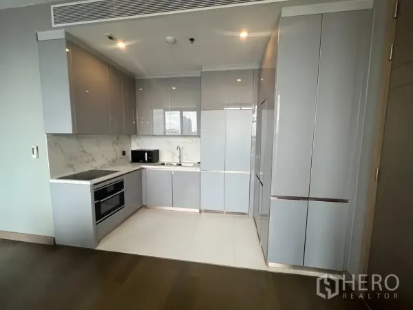 公寓 出租在Huai Khwang, Bangkok - 现代L形厨房，内置烤箱与炉灶，大理石挡板与通高柜体。