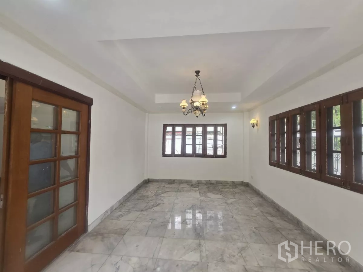 Detached House for rent in Phra Khanong, Bangkok - Bright living room with marble floors, chandelier and wood-framed windows in an On Nut area house.