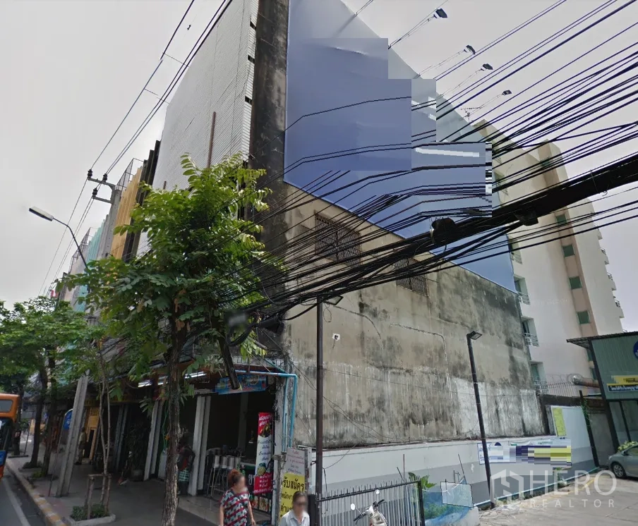 店屋 出租在Phra Khanong, Bangkok - 曼谷街巷转角的多层商铺外观，电线与行道树清晰可见。