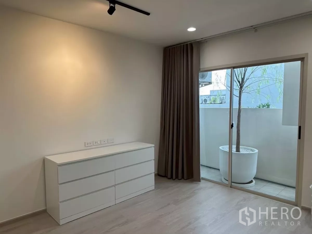 Townhouse for rent in Saphan Sung, Bangkok - Bedroom with sliding doors to a small balcony and dresser; large planter outside.