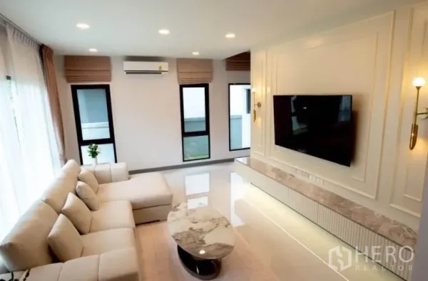 独立式住宅 出租在Bang Phli, Samut Prakan - 客厅配L型沙发、墙挂电视与大理石台面柜。