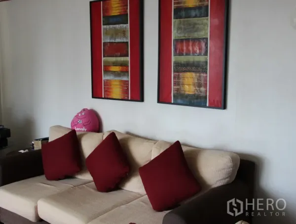 Condominium for rent in Khlong Toei, Bangkok - Cozy living room with a beige sofa, red cushions, and two abstract art paintings on the wall.