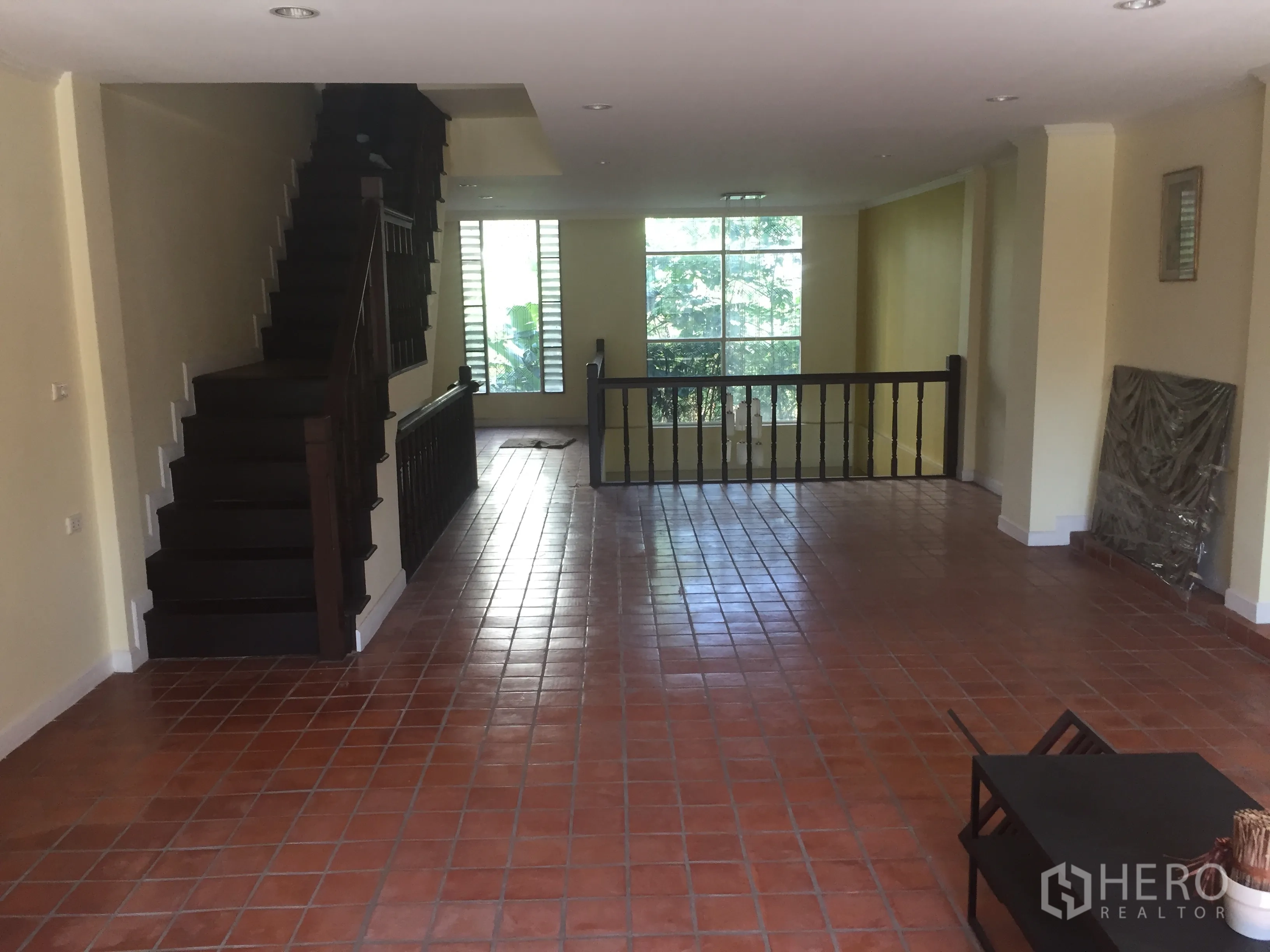 Townhouse for rent in Khlong Toei, Bangkok - Spacious split-level living area with terracotta tile floors, large window and a dark wood staircase.