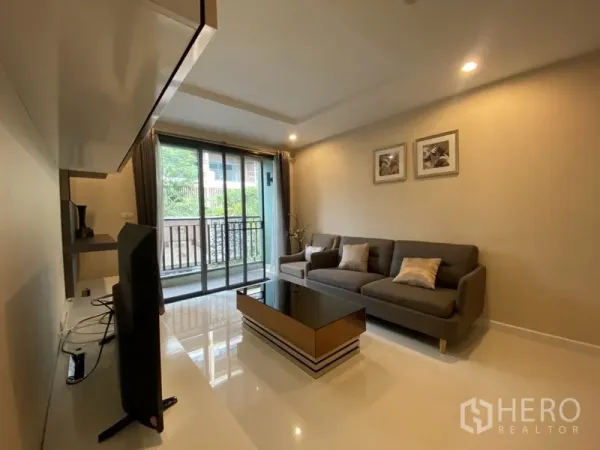 公寓 出租在Watthana, Bangkok - 采光充足的客厅，灰色沙发、电视柜，落地移门通向带绿景的阳台。