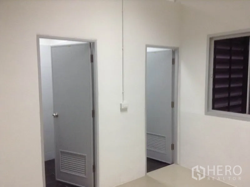 Warehouse for rent in Bang Kapi, Bangkok - Hallway with two gray doors to a bathroom and utility room plus a louvered window.