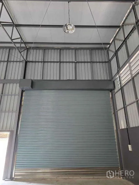 Warehouse for rent in Mueang Samut Sakhon, Samut Sakhon - Close-up of a tall roller shutter under a high warehouse ceiling and steel structure.
