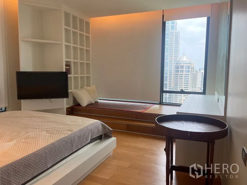 Condominium for rent in Pathum Wan, Bangkok - Bedroom with window seat, shelving, city view and wall-mounted TV.