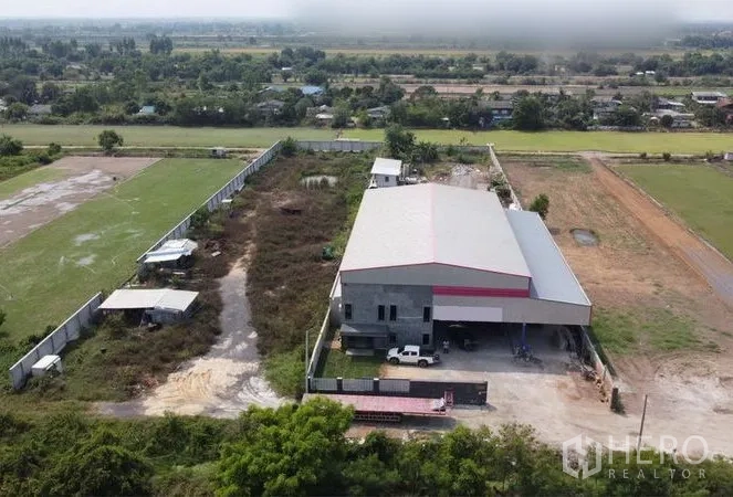 Warehouse for sale in Lam Luk Ka, Pathum Thani - Drone view showing a large fenced plot with open yard and the main warehouse building.