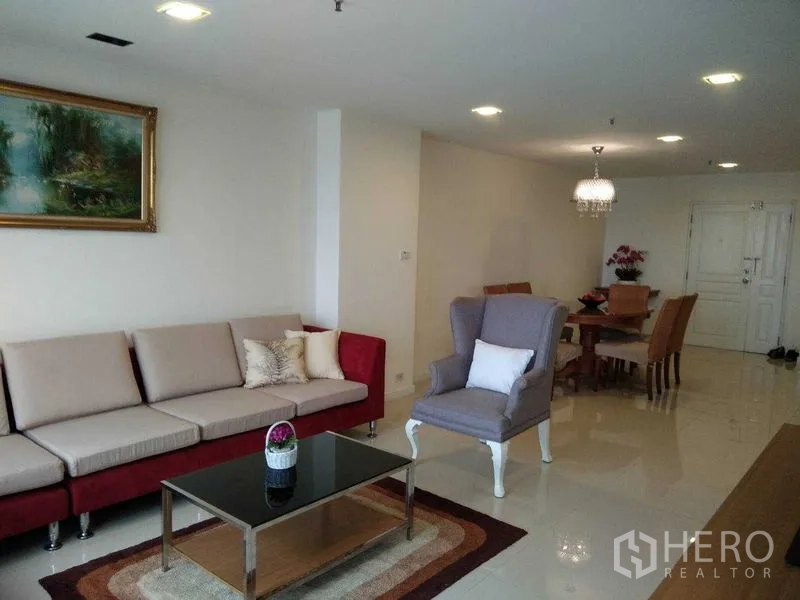 Condominium for rent in Khlong Toei, Bangkok - Spacious open-plan living and dining area with sofa, armchair, chandelier and glossy tile floors.