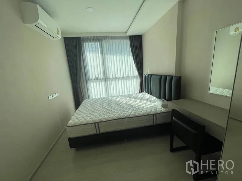 Condominium for rent in Khlong Toei, Bangkok - Second bedroom with upholstered headboard, desk, and wide window with curtains.